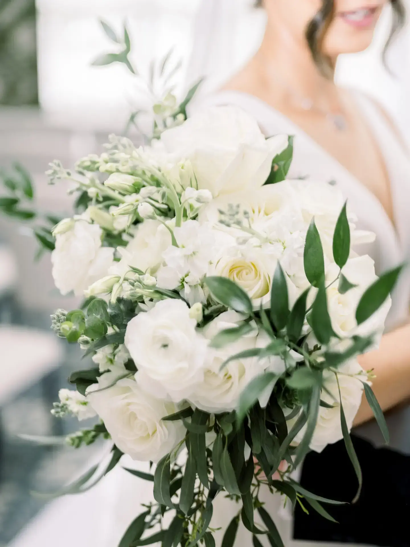 Bride holding a lush white rose bouquet with greenery and delicate floral accents.